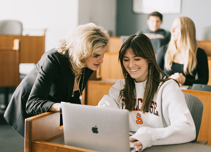 Professor helping student working on a laptop in a classroom