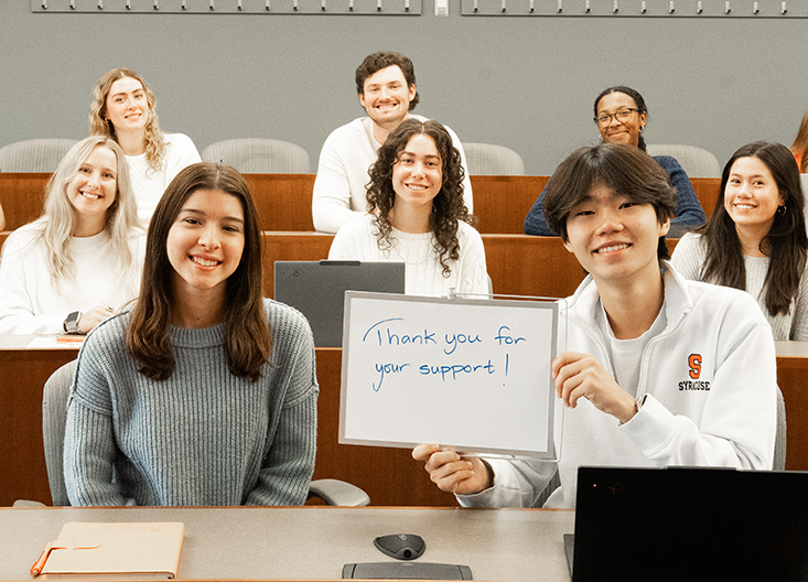 Students in classroom, one holding up a sign saying thank you for your support!