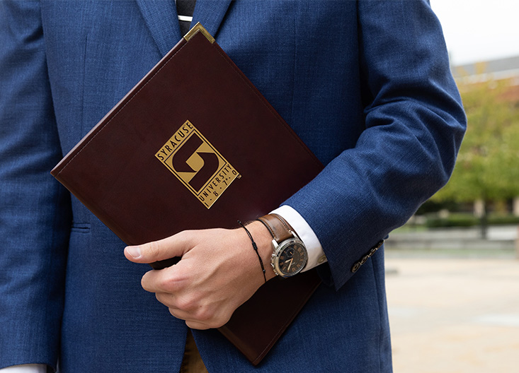 Student holding a Syracuse binder wearing a suit