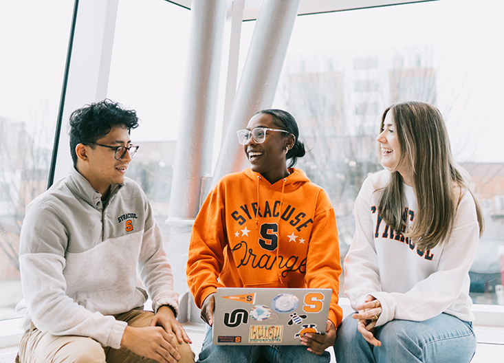 Three students laughing, sitting by a window