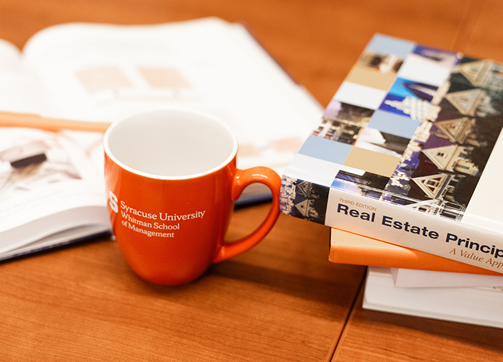 A few books lying on a table next to a Syracuse University mug