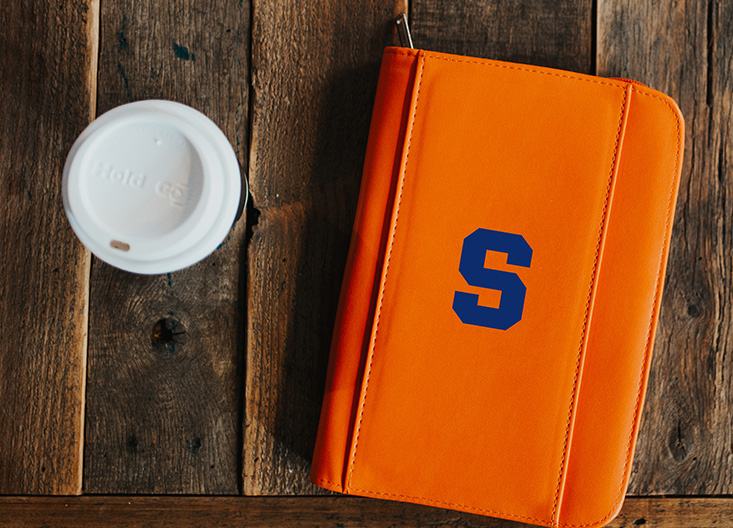 Coffee and a Syracuse notebook on table