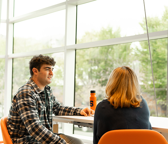 Two students chatting by window in Flaum grand hall