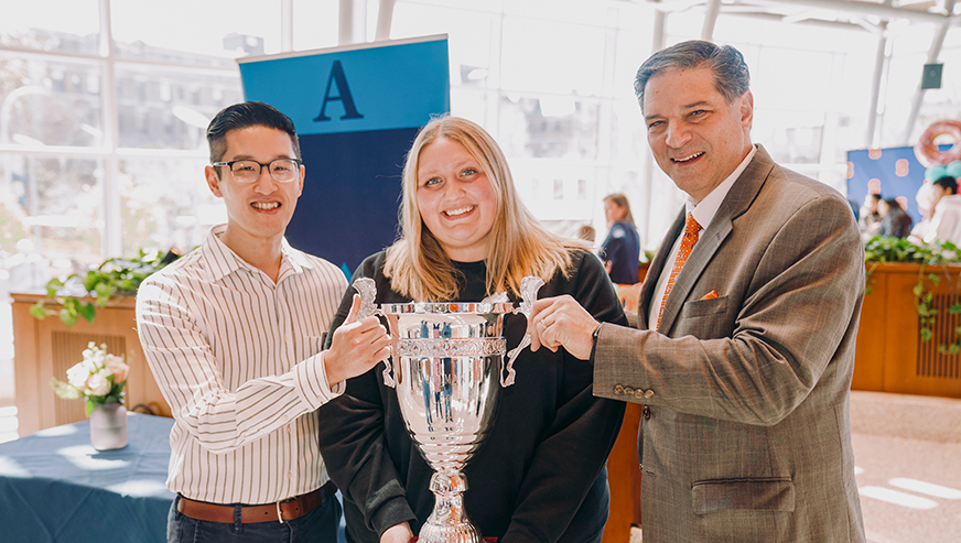 A student, staff member and professor posing with the Goodman Cup