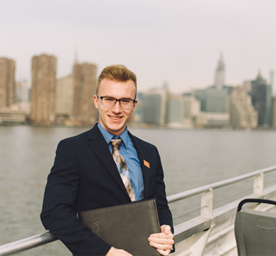 A professionally dressed student standing on a walkway over the water with a planner