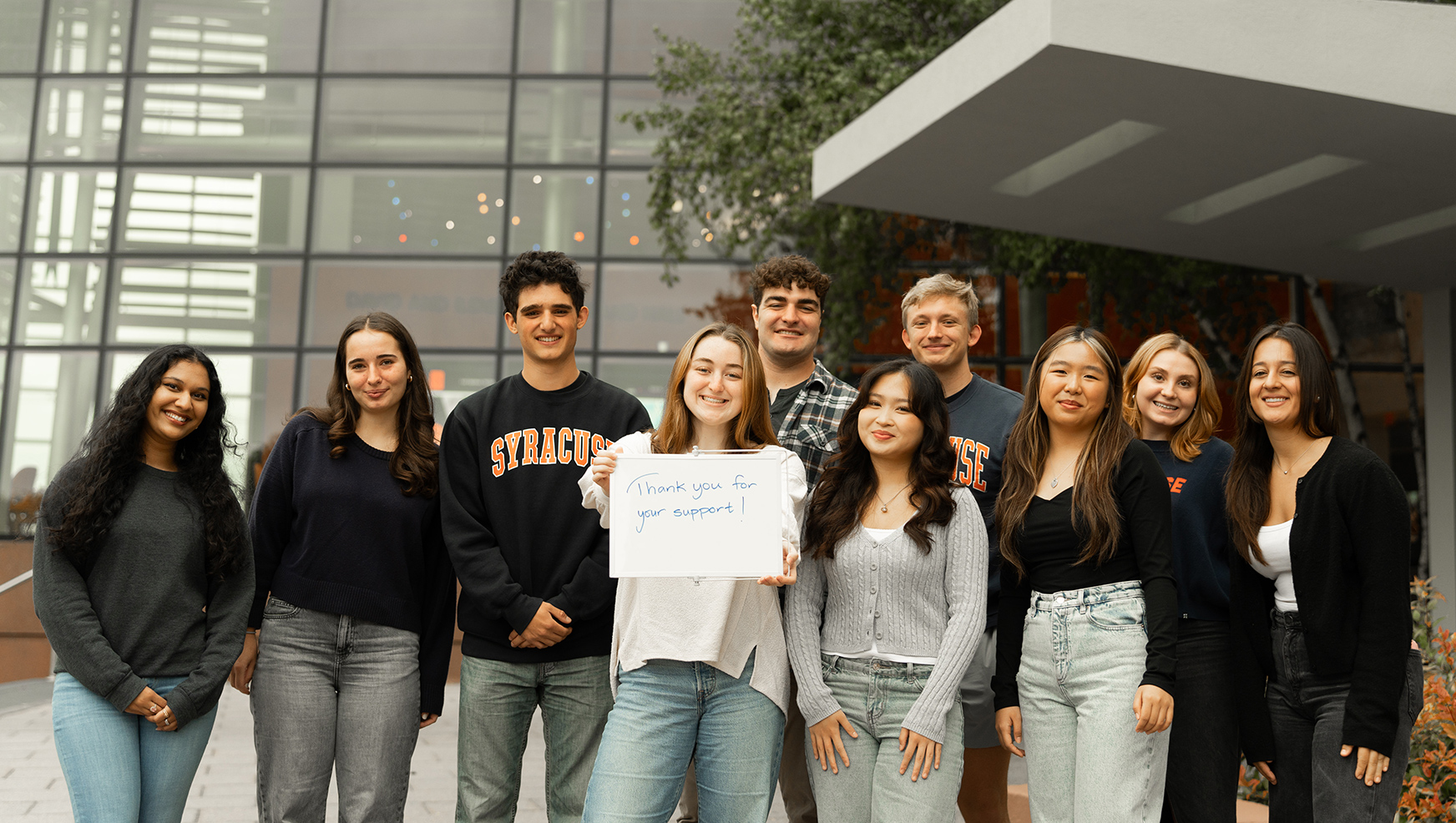 Group of students posing outside Whitman holding a sign saying